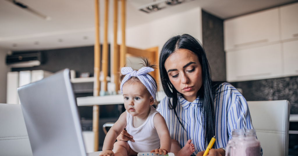 This shows a mother trying to work from home with her baby on the desk while she's on a laptop. The motherhood penalty at work
